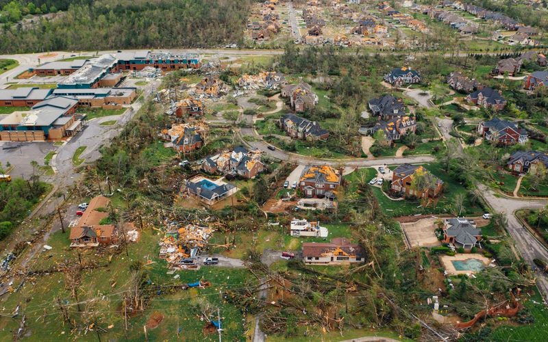 Aerial view of a neighborhood with storm-damaged roofs and debris